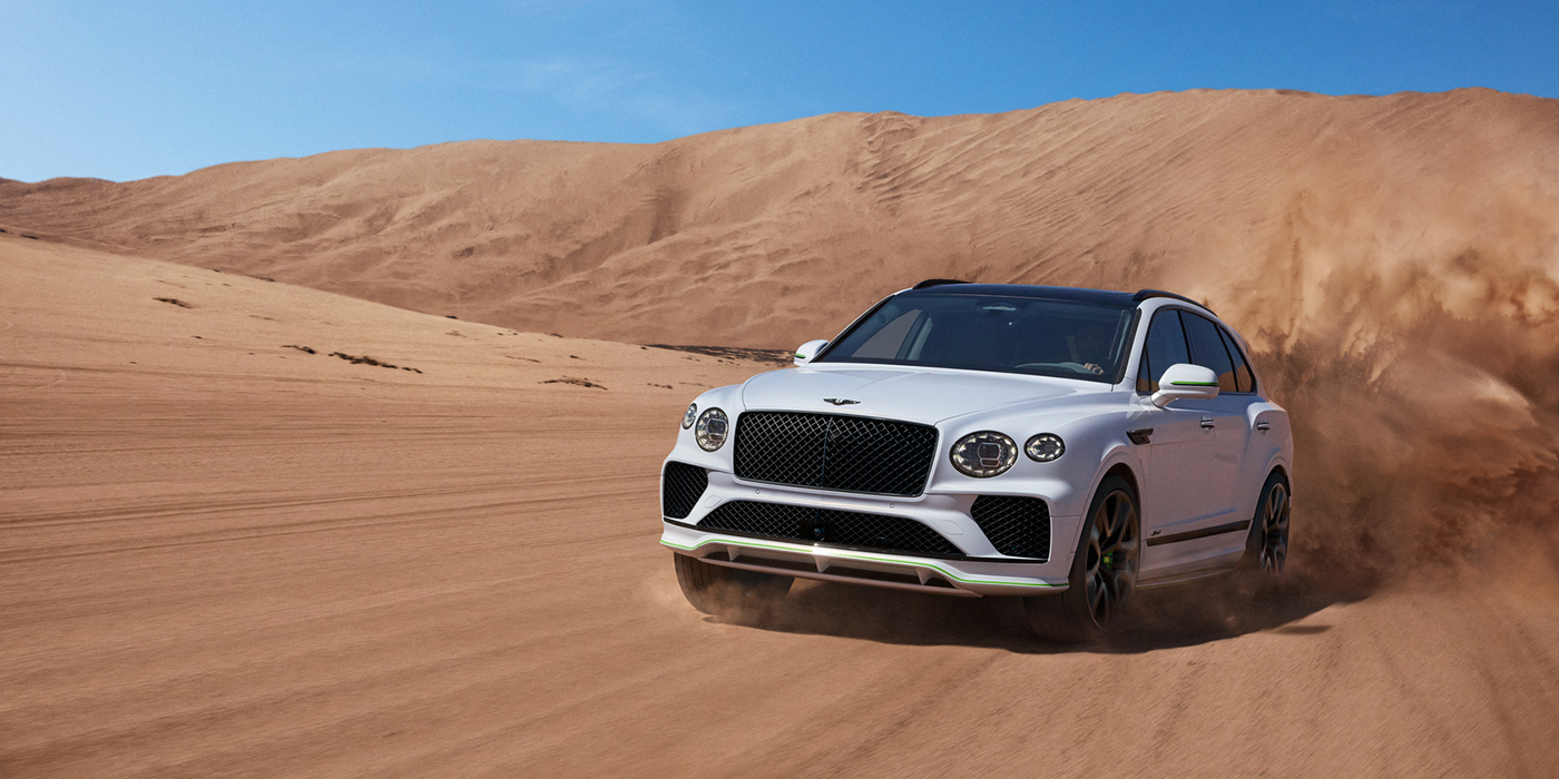 Bentley High Wycombe Bentley Bentayga Speed SUV front three quarter in Snow Quarts Pearlescent by Mulliner white paint driving dynamically through the desert