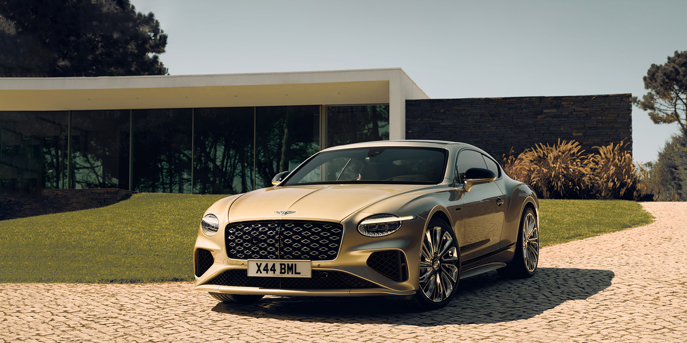 Bentley High Wycombe Bentley Continental GT Mulliner coupe front three quarters in Patina paint parked outside a glass fronted building with a grass lawn behind it
