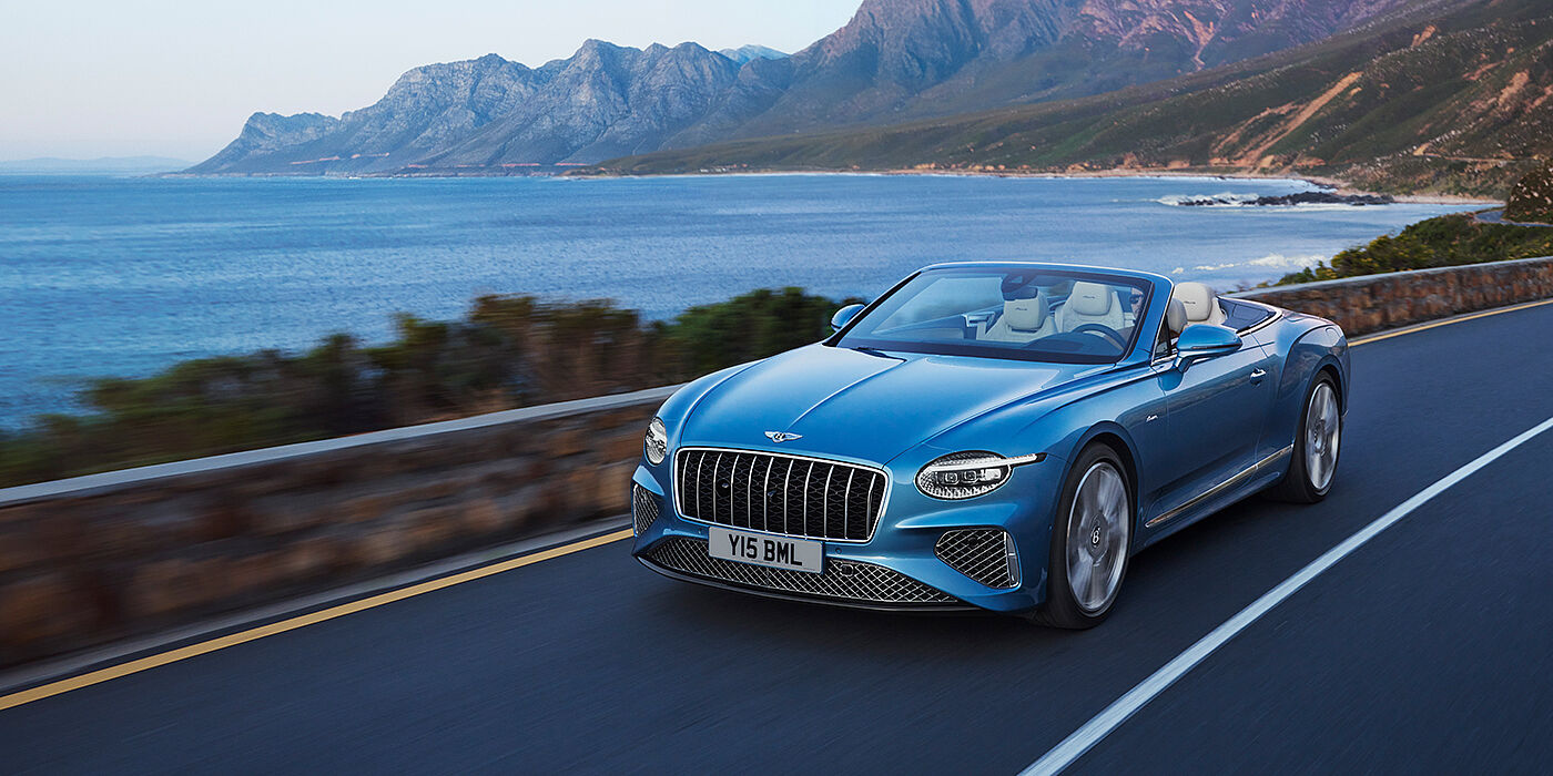 Bentley High Wycombe New Bentley Continental GTC Azure convertible in Light Windsor blue paint with 22 inch Azure wheels and chrome grill, driving dynamically by the sea