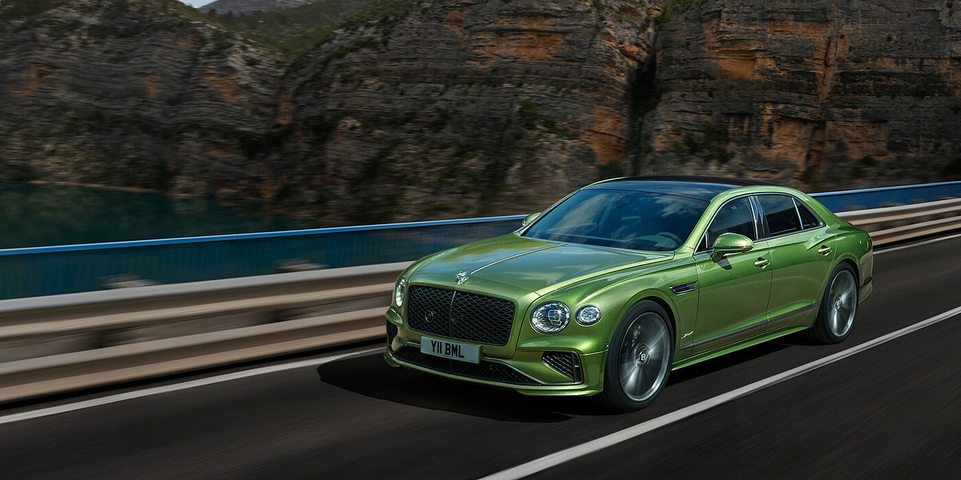 Bentley High Wycombe Bentley New Flying Spur Speed v8 hybrid sedan driving dynamically on a mountain road in Tourmaline Green paint
