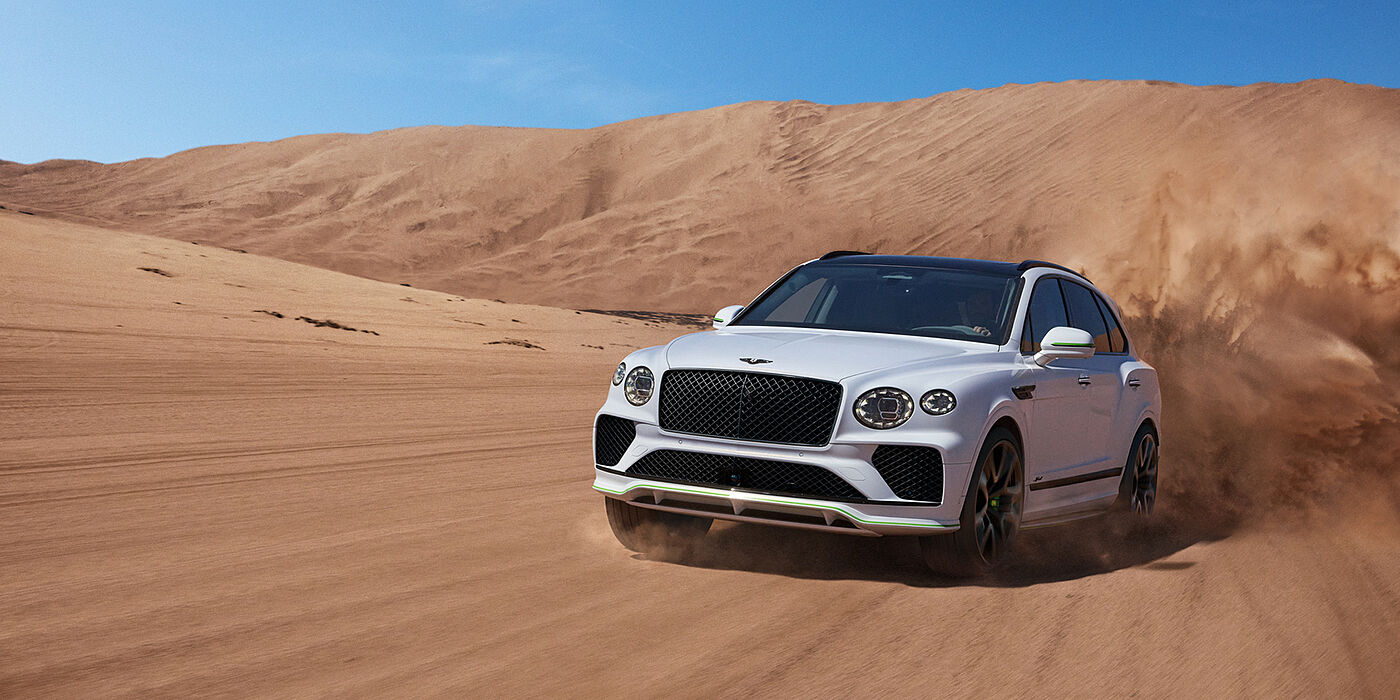 Bentley High Wycombe Bentley Bentayga Speed SUV front three quarter in Snow Quarts Pearlescent by Mulliner white paint driving dynamically through the desert