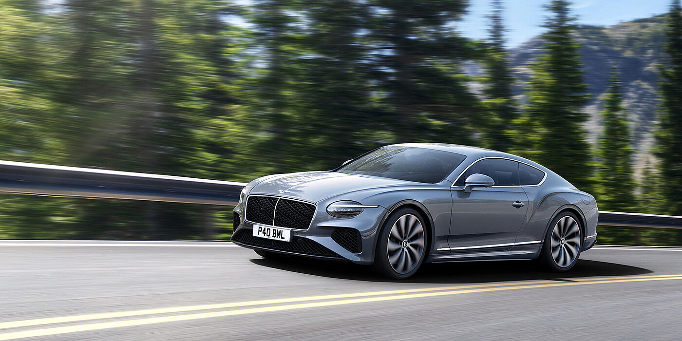 Bentley High Wycombe New Bentley Continental GT coupe in Silverlake paint and 22 inch ten-spoke wheels, driving dynamically on a tree-lined road in the sunshine