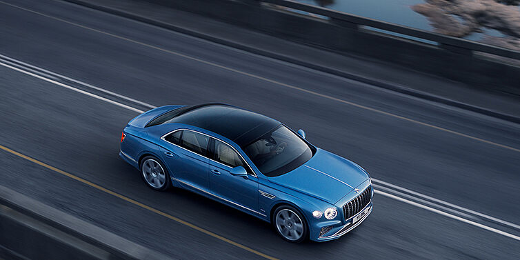 Bentley High Wycombe New Bentley Flying Spur Azure sedan in Light windsor blue paint by Mulliner, with 22 inch Azure wheels seen from overhead driving dynamically on a country road